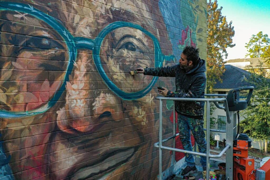 A man standing on a platform painting a Mural