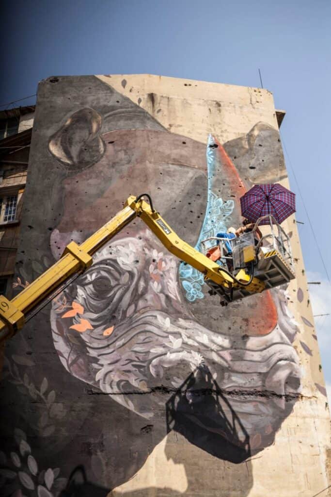 A man on a cherry picker painting a mural of a rhino